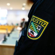 Gerichtssaal | Bildquelle: IMAGO, Jan Huebner Ärmel mit Logo eines Justizbeamten im Vordergrund, dahinter verschwommen der Gerichtssaal